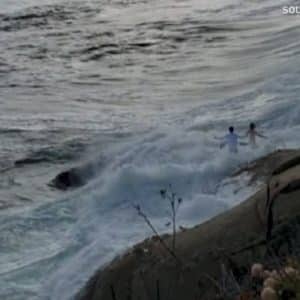 large wave sweeps couple into the ocean during their wedding photoshoot