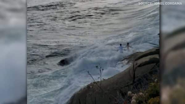 large wave sweeps couple into the ocean during their wedding photoshoot